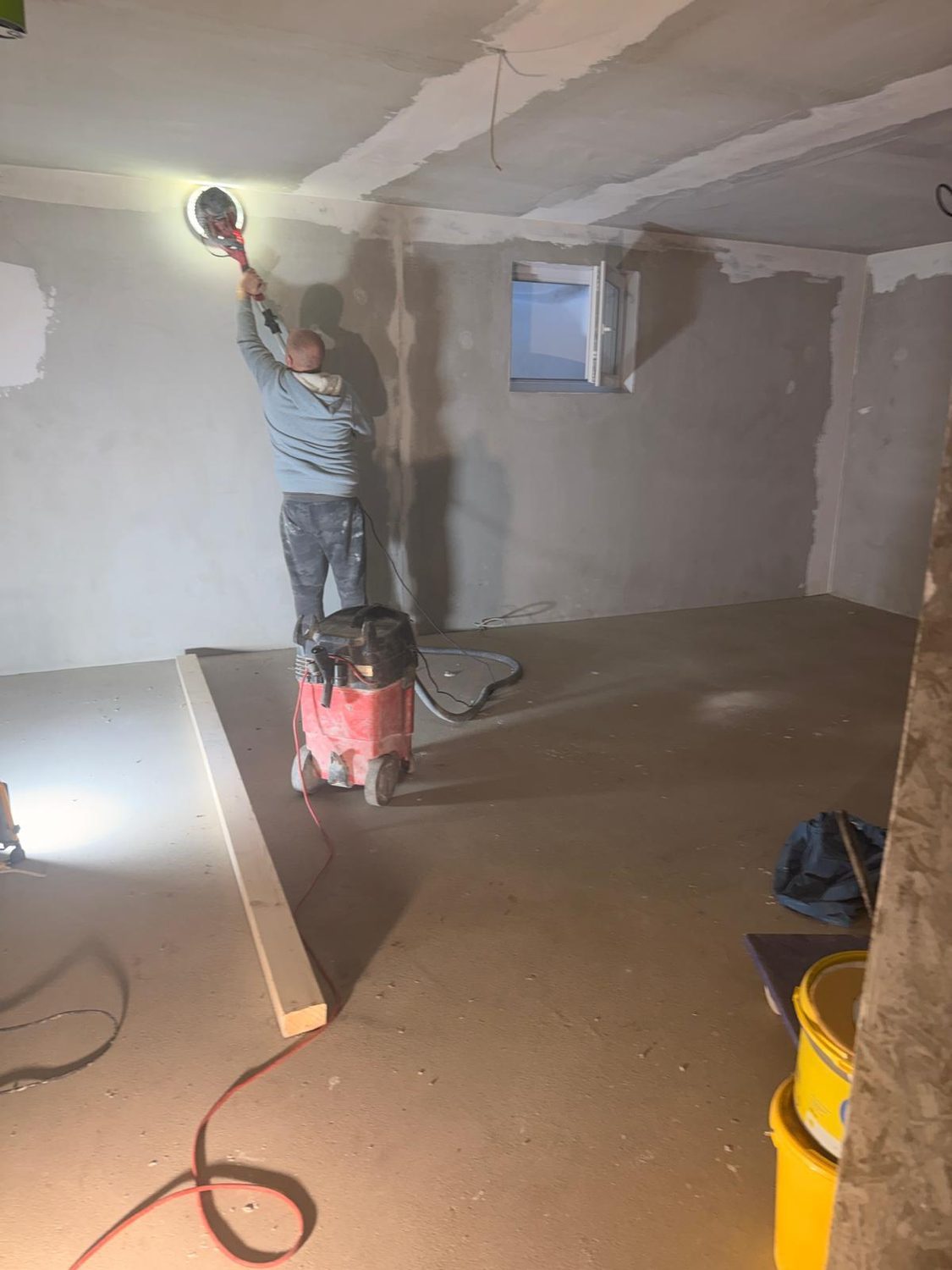 Handwerker schleift mit Langhalsschleifer und Absaugung den Wandanschluss zur Decke